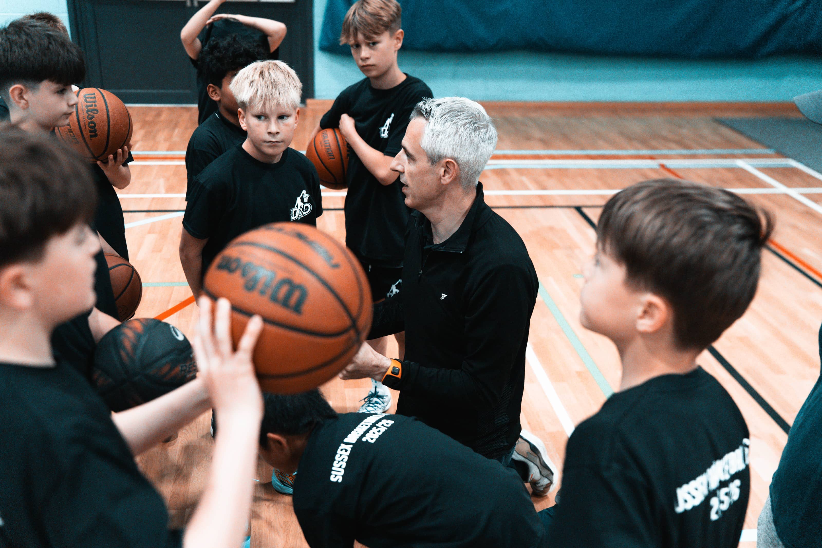 A basketball coach talking to his team of players gathered around him on the court