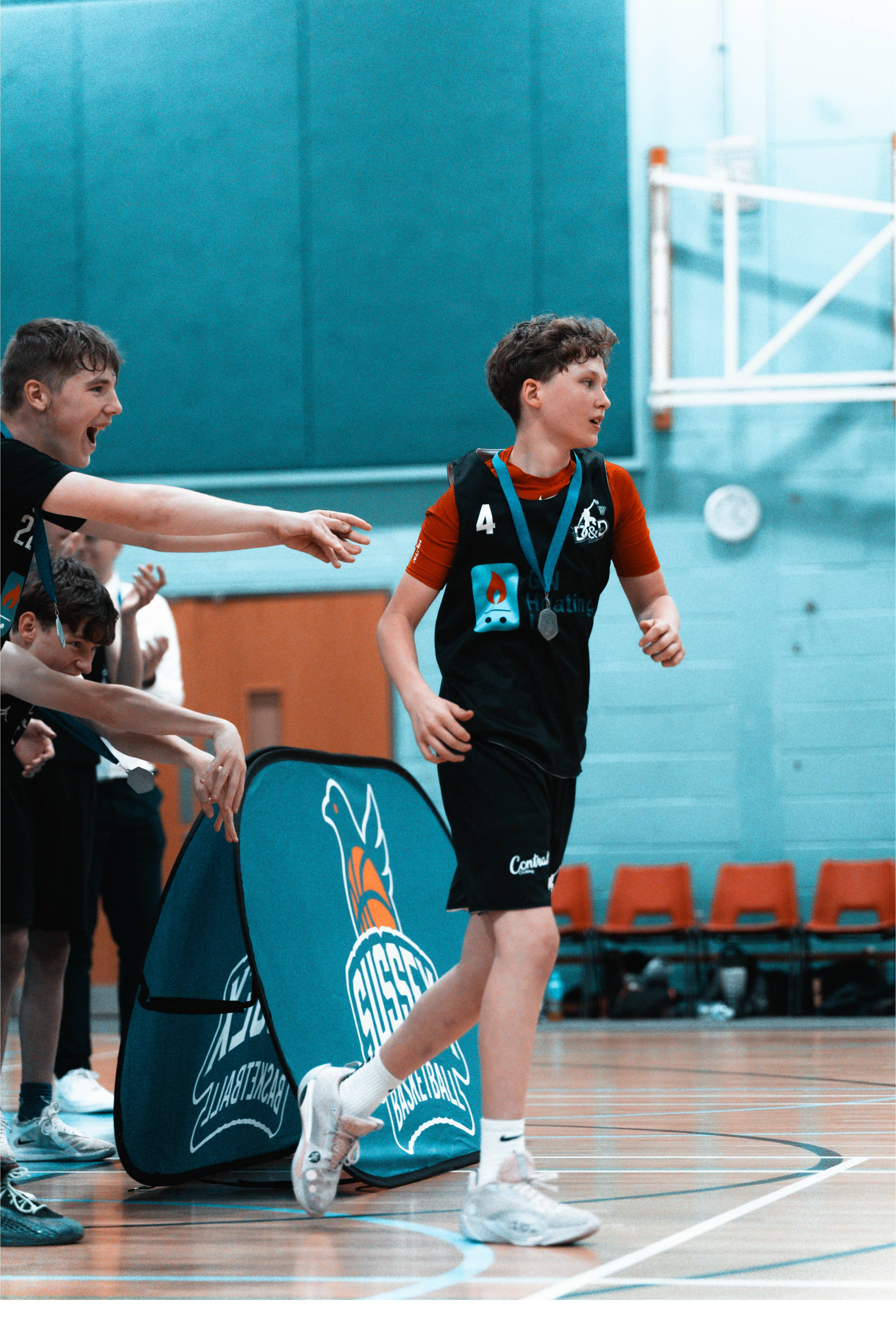 A basketball player wearing a medal and jersey number 4 running onto the court while teammates cheer and reach out to high-five him